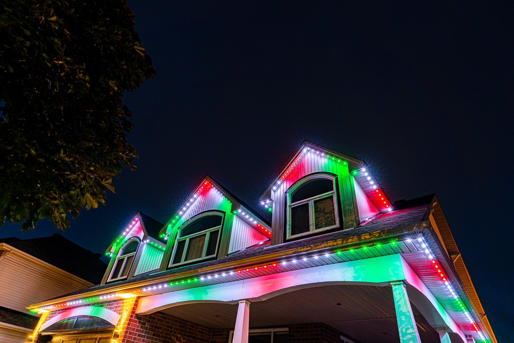 Permanent red, green and white Christmas lights on a two-story home's gables and porch