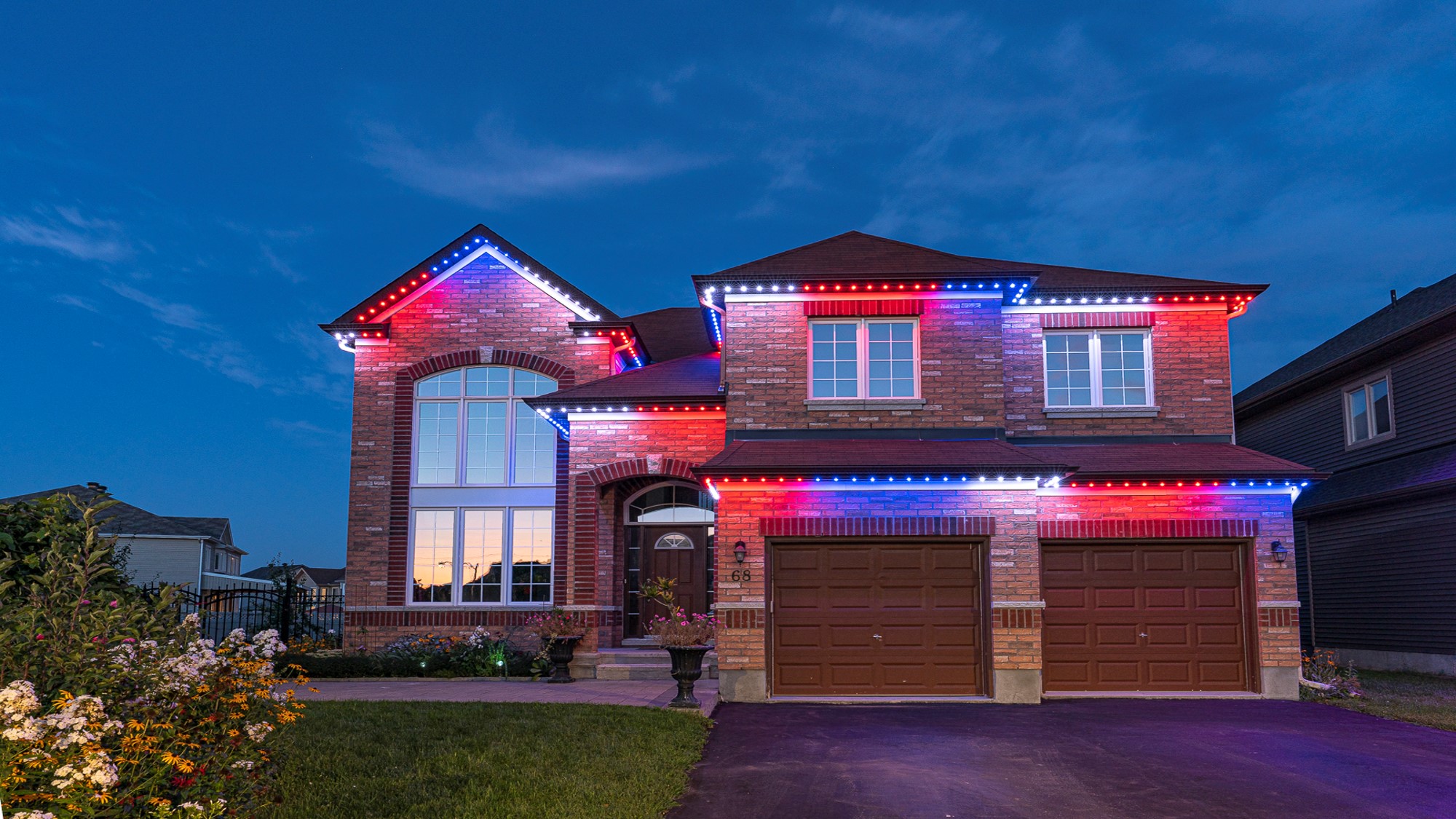 Permanent red, white and blue Fourth of July lights on a brick two-story home at dusk