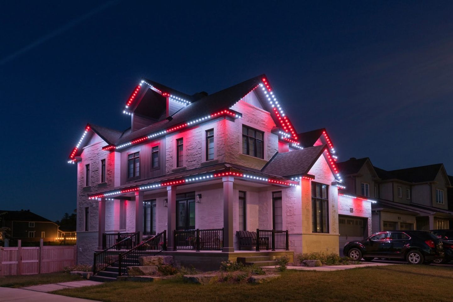 Permanent red and white Christmas lights on a two-story home at dusk