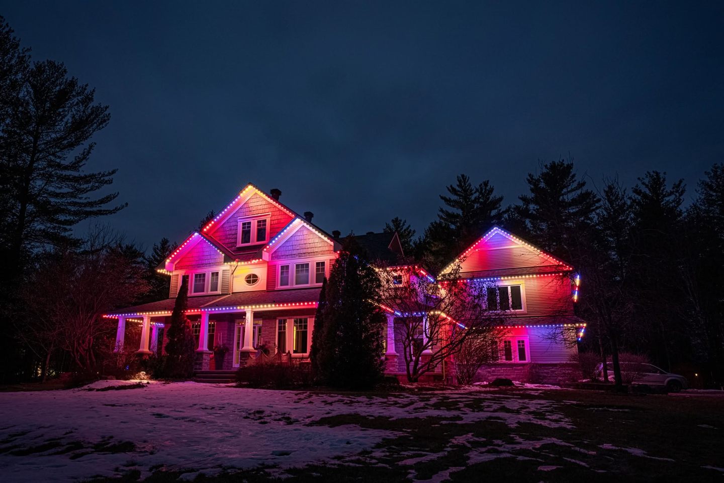 Permanent LED lights glowing on a home through winter snow at night