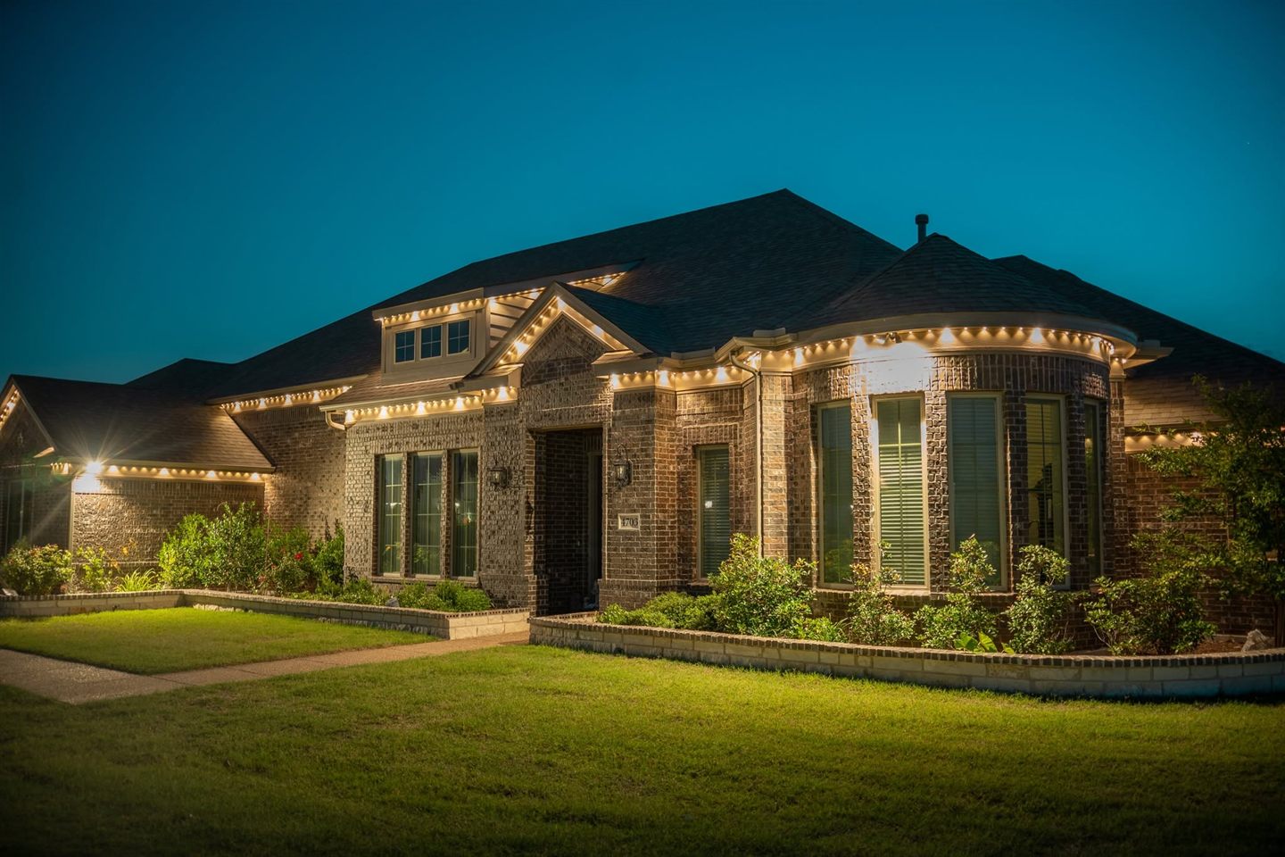 Permanent warm-white outdoor lights on a brick home, showing a clean professional roofline install