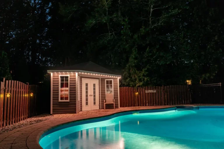 Backyard pool glows beside a shed lit with Brilliant By Night lighting