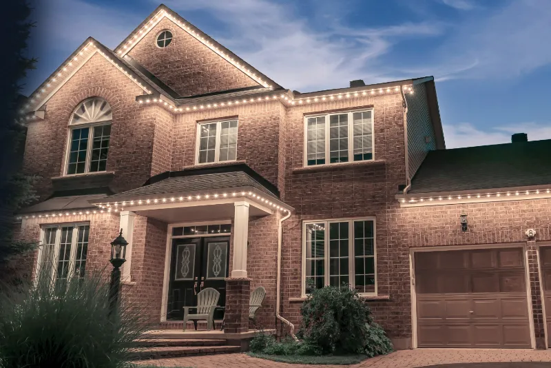 A two-story brick home with Brilliant By Night trim lighting illuminating the rooflines at night