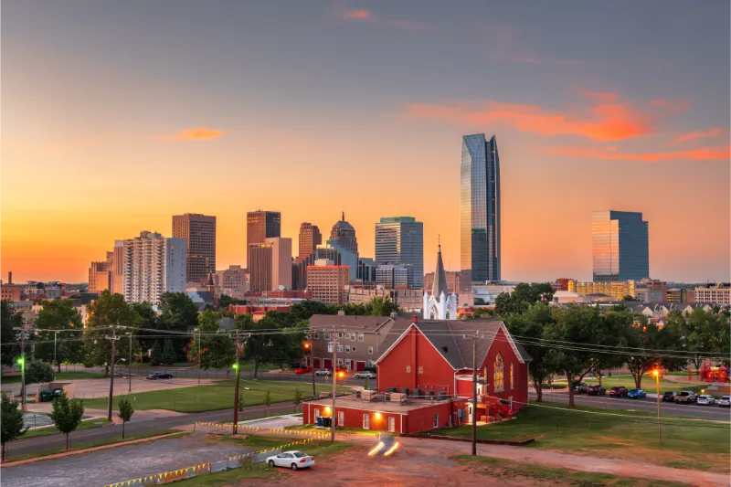 Sunset view of city skyline with tall buildings and a red church below in Oklahoma